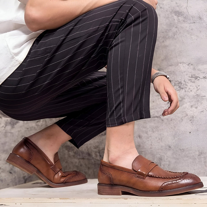 Homme accroupi portant un pantalon rayé noir et des chaussures en cuir marron de style mocassin. Détails de la couture et de la perforations des chaussures bien visibles., 45286724501685,45286724534453,45286724567221,45286724599989,45286724632757,45286724665525,45286724698293,45286724731061,45286724763829,45286724796597,45286724829365,45286724862133,45286724894901,45286724927669,45286724960437,45286724993205,45286725025973,45286725058741,45286725091509,45286725124277