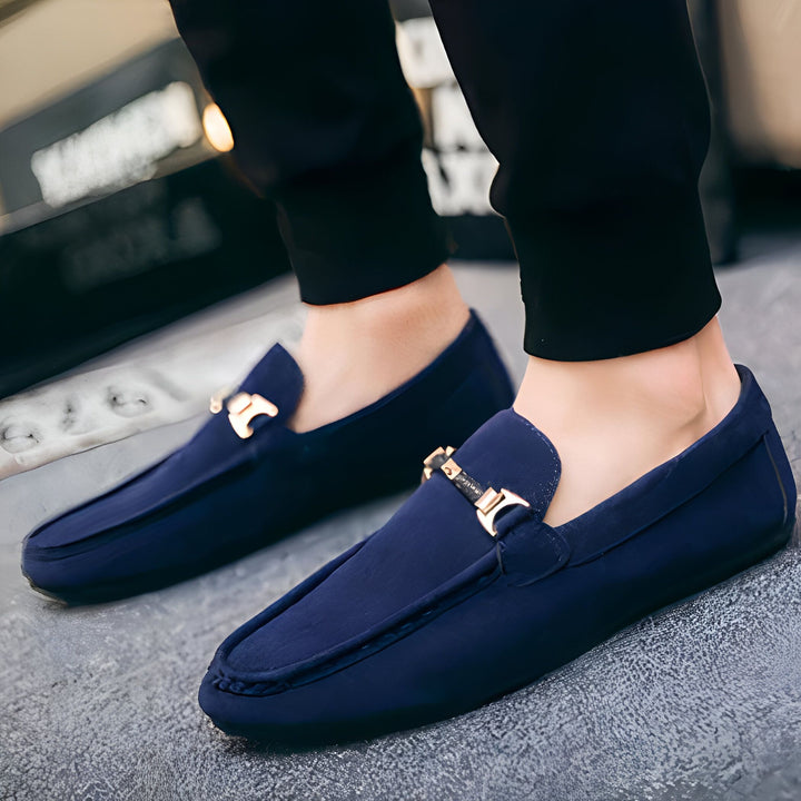 Gros plan sur des mocassins bleu marine en daim avec des ornements dorés portés par un homme. Élégance et confort pour un style décontracté chic. Chaussures parfaites pour toute occasion., 45287104807093,45287104839861,45287104872629,45287104905397,45287104938165,45287104970933,45287105003701,45287105036469,45287105069237