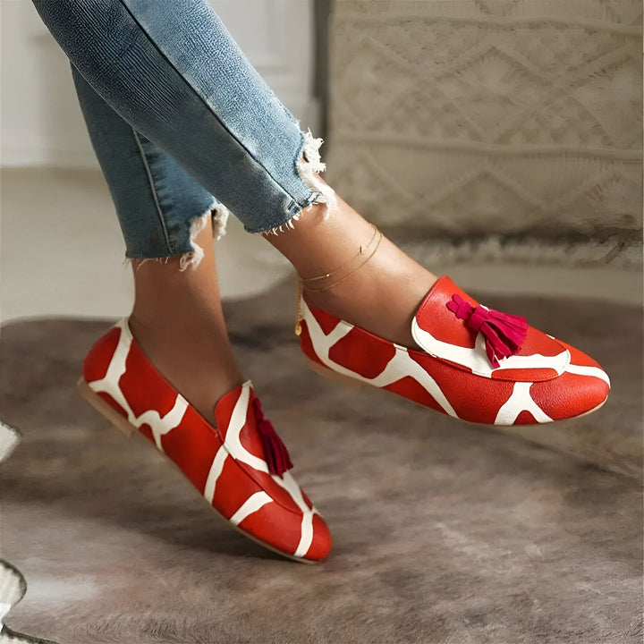 Chaussures mocassins rouges et blanches à motif girafe, avec des pompons rouges. Détail d'une cheville avec un fin bracelet doré. Jambes avec jean déchiré., 45286643171509,45286643204277,45286643237045,45286643269813,45286643302581,45286643335349,45286643368117,45286643400885,45286643433653