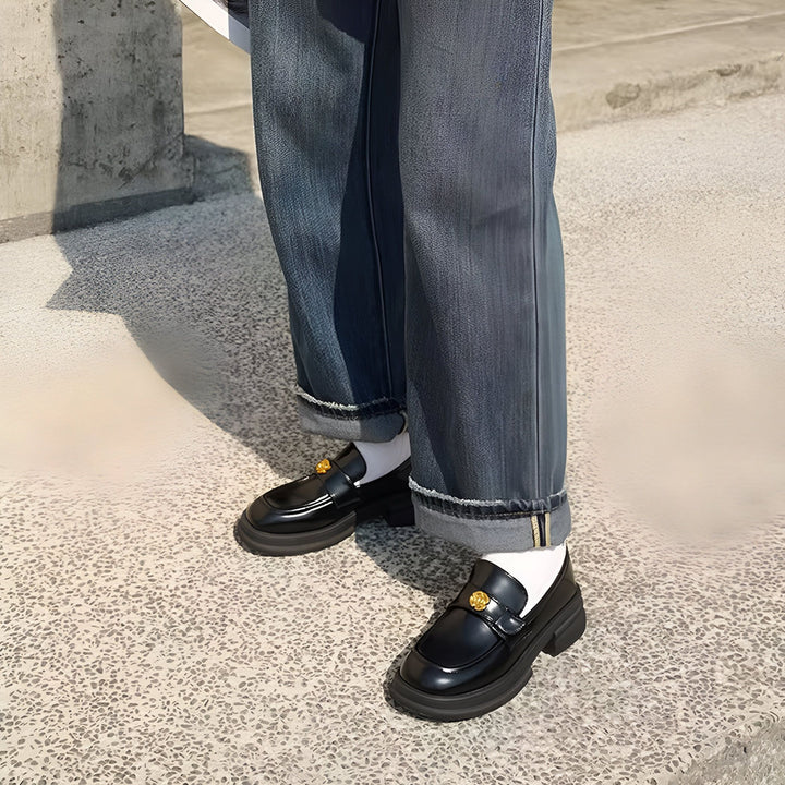 Personne portant un jean ample bleu et des mocassins noirs avec chaussettes blanches. Détails dorés sur les chaussures. Style décontracté et tendance., 45286630490293,45286630523061,45286630555829,45286630588597,45286630621365,45286630654133,45286630686901,45286630719669,45286630752437,45286630785205