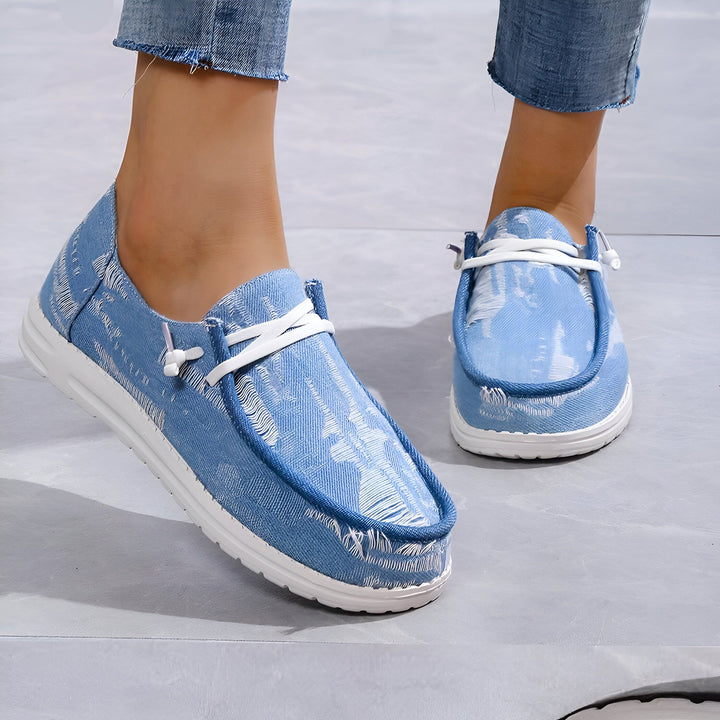 Gros plan sur des chaussures en toile bleu clair portées avec un jean. Chaussures décontractées à lacets blancs, parfaites pour un look estival., 45286736789685,45286736822453,45286736855221,45286736887989,45286736920757,45286736953525,45286736986293,45286737019061,45286737051829