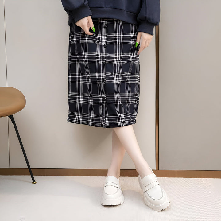 Image d'une personne portant une jupe à carreaux boutonnée associée à un pull bleu marine et des chaussures blanches à semelles épaisses. Une chaise moderne est visible en arrière-plan., 45286915899573,45286915932341,45286915965109,45286915997877,45286916030645,45286916063413,45286916096181,45286916128949,45286916161717,45286916194485,45286916227253,45286916260021,45286916292789,45286916325557,45286916358325,45286916391093