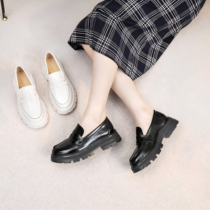 Une femme portant des mocassins noirs vernis à semelles épaisses. À côté d'elle, des mocassins blancs à semelles épaisses sont posés sur un tapis clair. La femme porte une jupe à carreaux., 45286915899573,45286915932341,45286915965109,45286915997877,45286916030645,45286916063413,45286916096181,45286916128949,45286916161717,45286916194485,45286916227253,45286916260021,45286916292789,45286916325557,45286916358325,45286916391093