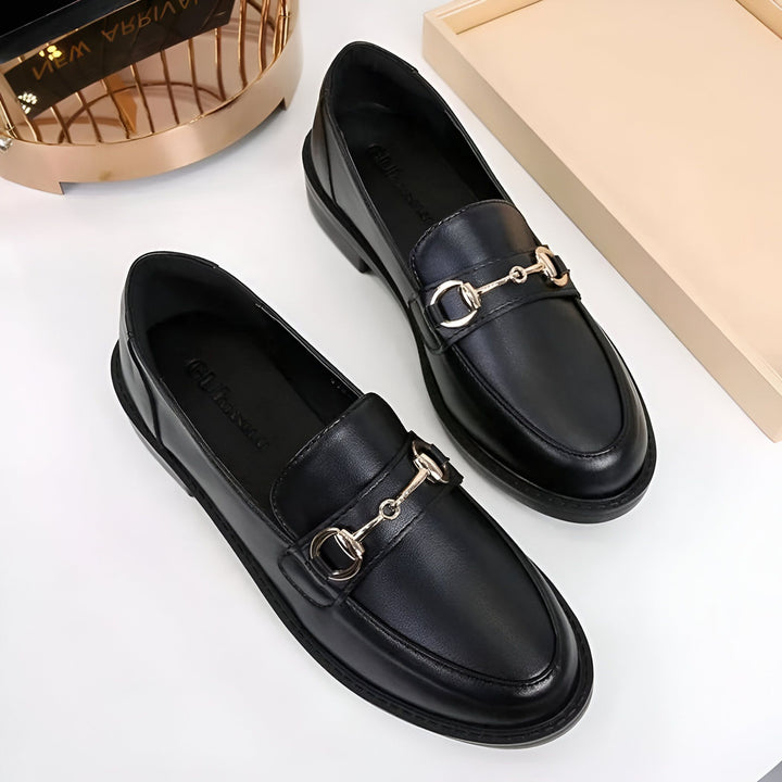 Deux mocassins noirs en cuir avec boucles dorées, posés sur une surface blanche à côté d'objets décoratifs dorés et beiges. Chaussures élégantes, mode féminine., 45286727844021,45286727876789,45286727909557,45286727942325,45286727975093,45286728007861,45286728040629,45286728073397,45286728106165