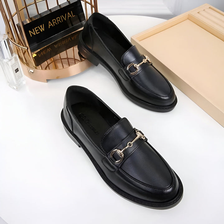 Deux mocassins noirs en cuir avec des boucles dorées sur le dessus, présentés à côté d'un parfum et d'un présentoir indiquant "Nouvelle Arrivée"., 45286727844021,45286727876789,45286727909557,45286727942325,45286727975093,45286728007861,45286728040629,45286728073397,45286728106165