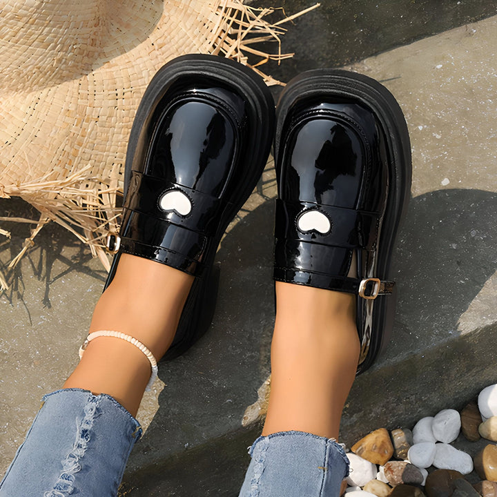 Vue plongeante de chaussures vernies noires avec boucle et détail cœur, portées avec un jean et une chaîne de cheville. Chapeau de paille visible., 45286866419893,45286866452661,45286866485429,45286866518197,45286866550965,45286866583733