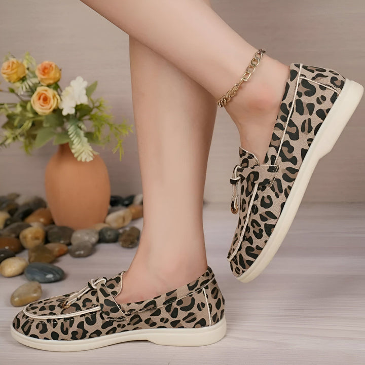 Chaussures plates à motif léopard portées par une femme avec une chaîne de cheville. Arrière-plan flou avec vase et cailloux., 45286648250549,45286648283317,45286648316085,45286648348853,45286648381621,45286648414389,45286648447157,45286648479925