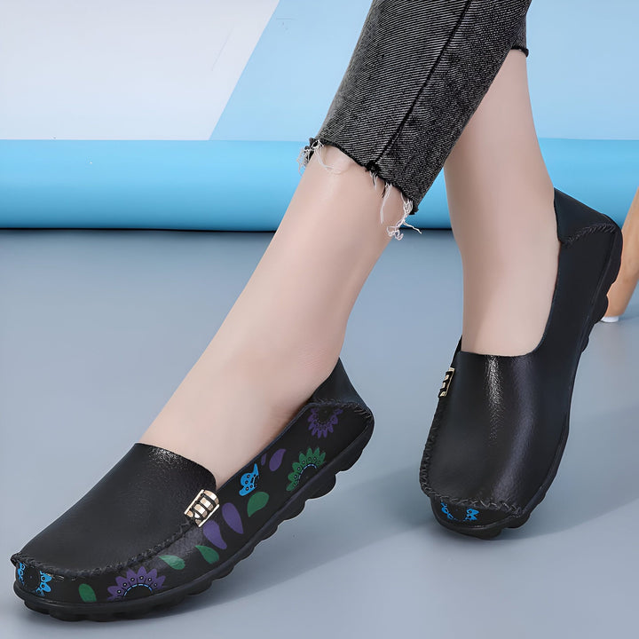 Chaussures plates noires en cuir portées par une femme, avec un motif floral coloré sur les côtés et une boucle décorative. Vêtue d'un jean gris effiloché., 45286851346613,45286851379381,45286851412149,45286851444917,45286851477685,45286851510453,45286851543221,45286851575989,45286851608757,45286851641525,45286851674293,45286851707061,45286851739829,45286851772597,45286851805365,45286851838133,45286851870901,45286851903669,45286851936437,45286851969205,45286852001973,45286852034741,45286852067509,4