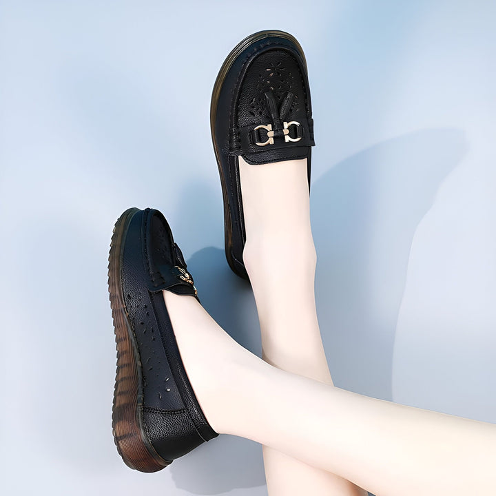 Deux mocassins noirs en cuir sur pieds féminins, sur fond bleu clair. Chaussures élégantes avec détails décoratifs dorés et perforations. Idéal pour un look décontracté et confortable., 45287000506549,45287000539317,45287000572085,45287000604853,45287000637621,45287000670389,45287000703157,45287000735925,45287000768693,45287000801461,45287000834229,45287000866997,45287000899765,45287000932533,45287000965301,45287000998069,45287001030837,45287001063605,45287001096373,45287001129141,45287001161909,