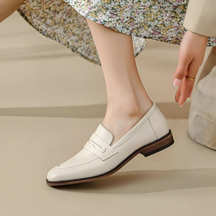 Gros plan sur une femme portant des mocassins blancs en cuir. La chaussure est classique avec une semelle en bois foncée. La femme porte une robe fleurie et une bague dorée. Mode, style., 45286733414581,45286733447349,45286733480117,45286733512885,45286733545653,45286733578421,45286733611189