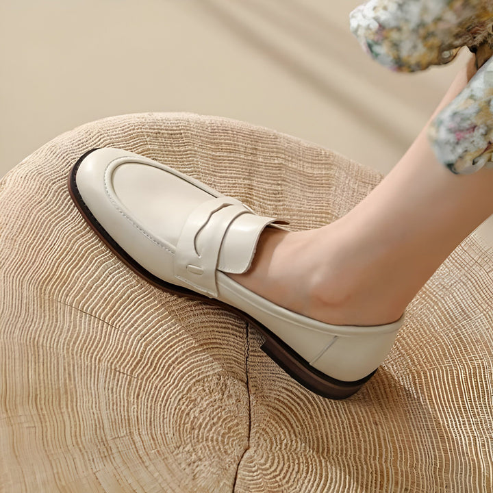 Gros plan sur un mocassin en cuir crème porté par une femme assise sur une souche d'arbre. Détail du cuir lisse et de la semelle foncée. Idée de look décontracté., 45286733414581,45286733447349,45286733480117,45286733512885,45286733545653,45286733578421,45286733611189