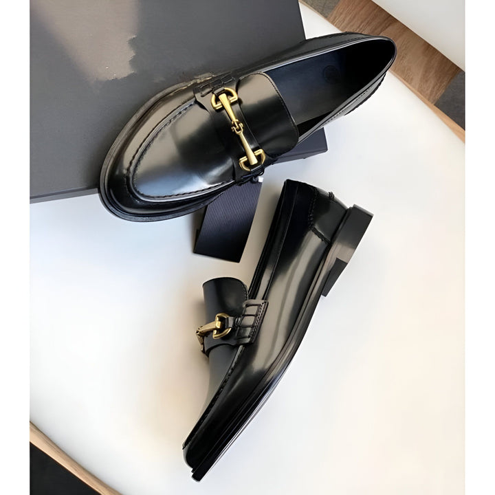 Vue rapprochée de deux mocassins noirs en cuir verni avec une boucle dorée, présentés sur une surface blanche avec une boîte noire en arrière-plan., 45286727188661,45286727221429,45286727254197,45286727286965,45286727319733,45286727352501