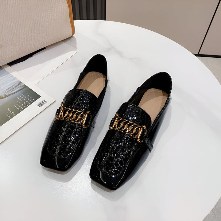 Vue rapprochée de deux mocassins noirs vernis avec un motif peau de crocodile et une chaîne dorée. Les chaussures sont sur une table blanche à côté d'un magazine et d'un sac à main., 45286865436853,45286865469621,45286865502389,45286865535157,45286865567925,45286865600693,45286865633461,45286865666229,45286865698997,45286865731765,45286865764533,45286865797301,45286865830069,45286865862837
