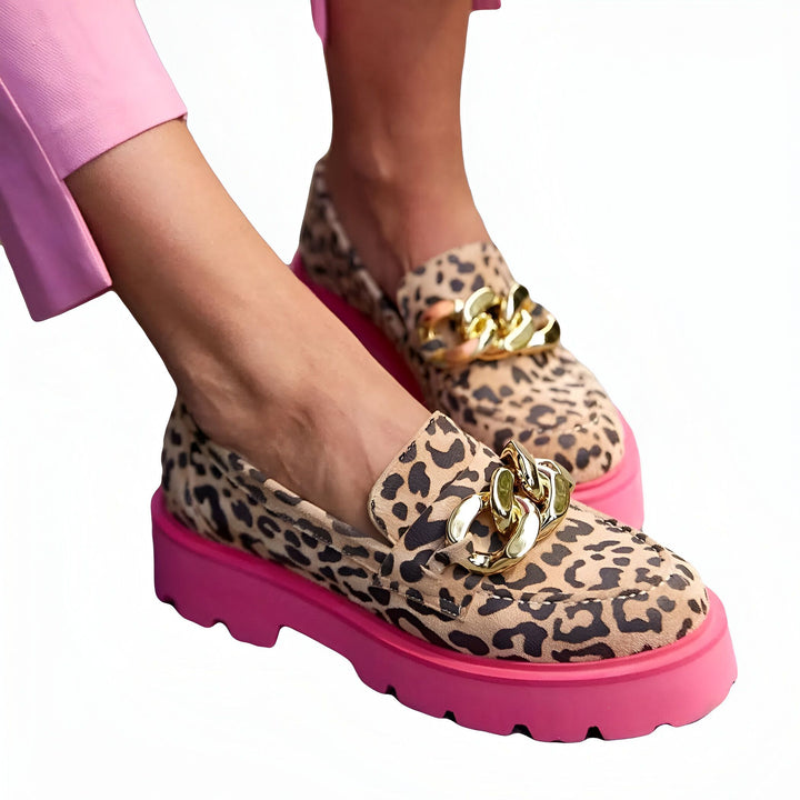 Chaussures mocassins léopard avec chaîne dorée et semelle rose, portées par une personne en pantalon rose. Ces chaussures combinent un motif animal audacieux avec des détails modernes., 45286832406709,45286832439477,45286832472245,45286832505013,45286832537781,45286832570549,45286832603317,45286832636085