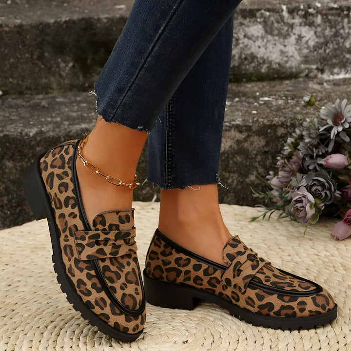 Gros plan sur des mocassins à imprimé léopard portés avec un jean bleu foncé et une chaîne de cheville dorée. Chaussures tendance sur un tapis en paille., 45286625870005,45286625902773,45286625935541,45286625968309,45286626001077,45286626033845,45286626066613,45286626099381