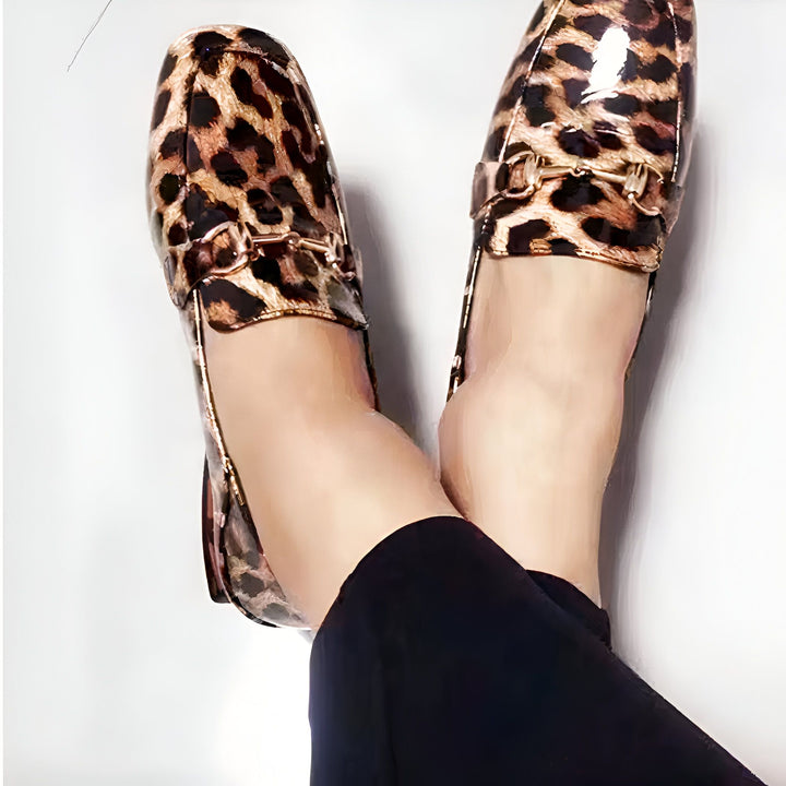 Gros plan sur des mocassins vernis à imprimé léopard portés avec un pantalon noir, jambes croisées sur fond blanc. Détails dorés sur les chaussures., 45287153991861,45287154024629,45287154057397,45287154090165,45287154122933,45287154155701