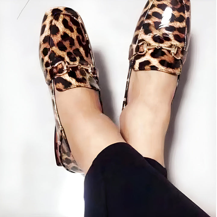 Deux pieds croisés portant des mocassins en cuir verni à motif léopard avec des ornements dorés, sur un fond blanc., 45287153991861,45287154024629,45287154057397,45287154090165,45287154122933,45287154155701