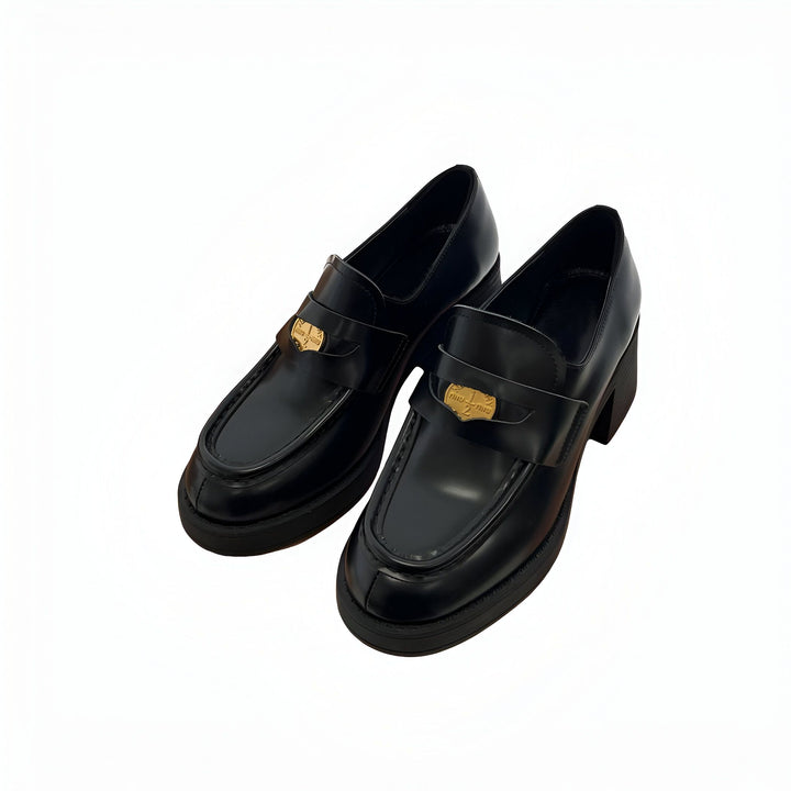 Paire de mocassins noirs à plateforme avec un ornement doré de la marque Miu Miu sur une surface blanche. Chaussures élégantes, chaussures de luxe, mode féminine., 45286900596917,45286900629685,45286900662453,45286900695221,45286900727989