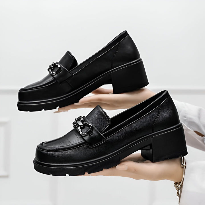 Deux mocassins noirs à talons épais, ornés d'une chaîne argentée, présentés sur les mains d'une personne. Chaussures élégantes et modernes, parfaites pour un look tendance., 45286687834293,45286687867061,45286687899829,45286687932597,45286687965365,45286687998133,45286688030901