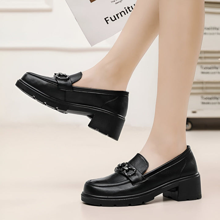 Gros plan sur une femme portant des mocassins noirs à talons épais avec ornements métalliques. Chaussures élégantes et confortables pour un look tendance., 45286687834293,45286687867061,45286687899829,45286687932597,45286687965365,45286687998133,45286688030901