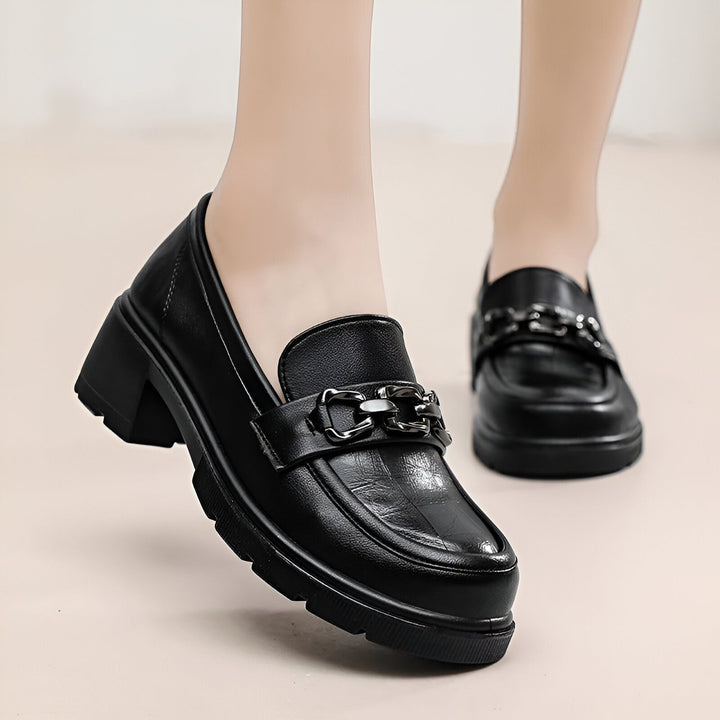 Gros plan sur des mocassins noirs en cuir avec des talons épais et une chaîne décorative sur le dessus. Chaussures de mode pour femmes., 45286687834293,45286687867061,45286687899829,45286687932597,45286687965365,45286687998133,45286688030901