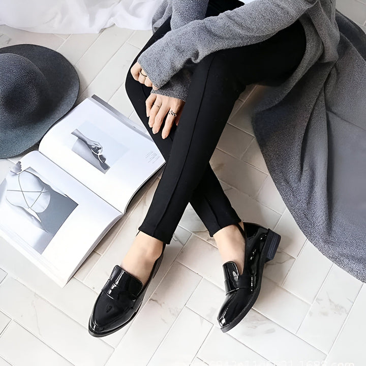 Femme assise sur le sol carrelé avec des chaussures noires vernies. Elle porte un pantalon noir et un cardigan gris. Un livre ouvert et un chapeau gris sont à côté d'elle., 45286720340149,45286720372917,45286720405685,45286720438453,45286720471221,45286720503989,45286720536757,45286720569525,45286720602293,45286720635061