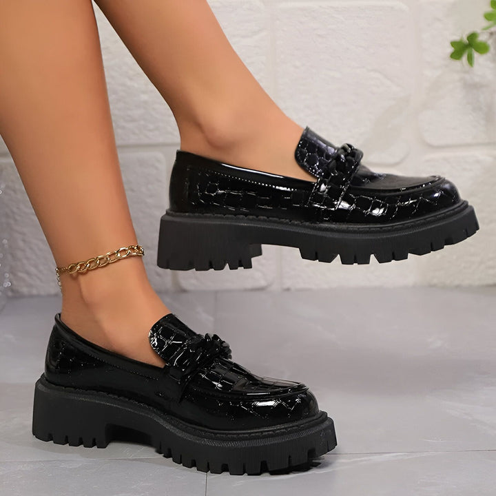 Gros plan de chaussures mocassins noires à plateforme, avec un motif croco verni et une chaîne décorative. Portées avec une chaîne de cheville dorée., 45286688063669,45286688096437,45286688129205,45286688161973,45286688194741,45286688227509,45286688260277,45286688293045