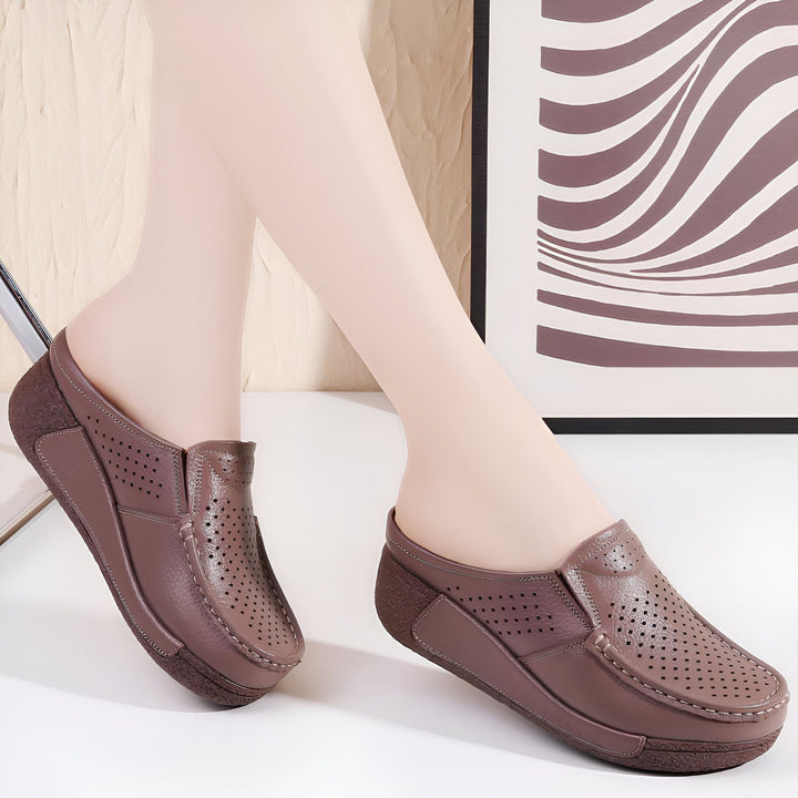 Image de deux mules en cuir marron avec des perforations, portées par un mannequin. Les chaussures ont une semelle compensée et une allure décontractée., 45286790791349,45286790824117,45286790856885,45286790889653,45286790922421,45286790955189,45286790987957,45286791020725,45286791053493,45286791086261,45286791119029,45286791151797,45286791184565,45286791217333,45286791250101,45286791282869,45286791315637,45286791348405,45286791381173,45286791413941,45286791446709,45286791479477,45286791512245,4528679
