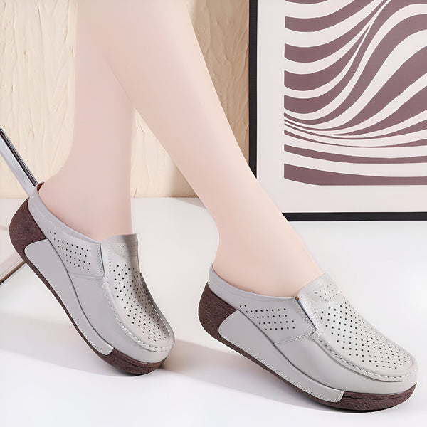 Gros plan de mules grises en cuir avec motifs perforés, portées par une femme. Chaussures d'intérieur confortables avec semelle compensée marron., 45286790791349,45286790824117,45286790856885,45286790889653,45286790922421,45286790955189,45286790987957,45286791020725,45286791053493,45286791086261,45286791119029,45286791151797,45286791184565,45286791217333,45286791250101,45286791282869,45286791315637,45286791348405,45286791381173,45286791413941,45286791446709,45286791479477,45286791512245,45286791545013