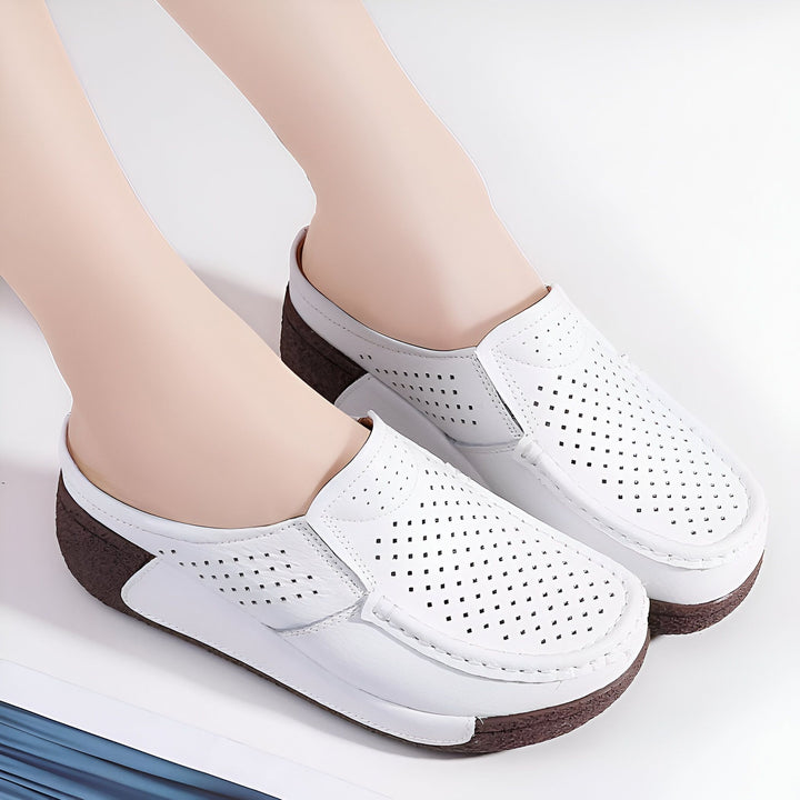 Vue rapprochée de pieds chaussés de mules blanches en cuir perforé. Chaussures d'été confortables avec semelle marron. Idéales pour le printemps ou les beaux jours., 45286790791349,45286790824117,45286790856885,45286790889653,45286790922421,45286790955189,45286790987957,45286791020725,45286791053493,45286791086261,45286791119029,45286791151797,45286791184565,45286791217333,45286791250101,45286791282869,45286791315637,45286791348405,45286791381173,45286791413941,45286791446709,45286791479477,45286791