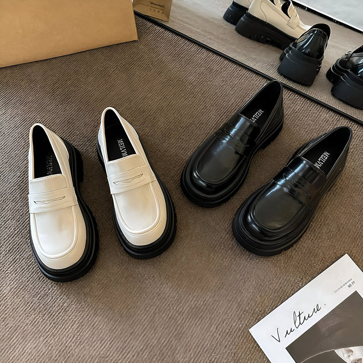 Gros plan de mocassins à semelles épaisses noirs et blancs, posés sur un tapis texturé. On distingue également un magazine "Vulture" et un sac en papier en arrière-plan. Mise en scène de chaussures tendance., 45286864093365,45286864126133,45286864158901,45286864191669,45286864224437,45286864257205,45286864289973,45286864322741,45286864355509,45286864388277