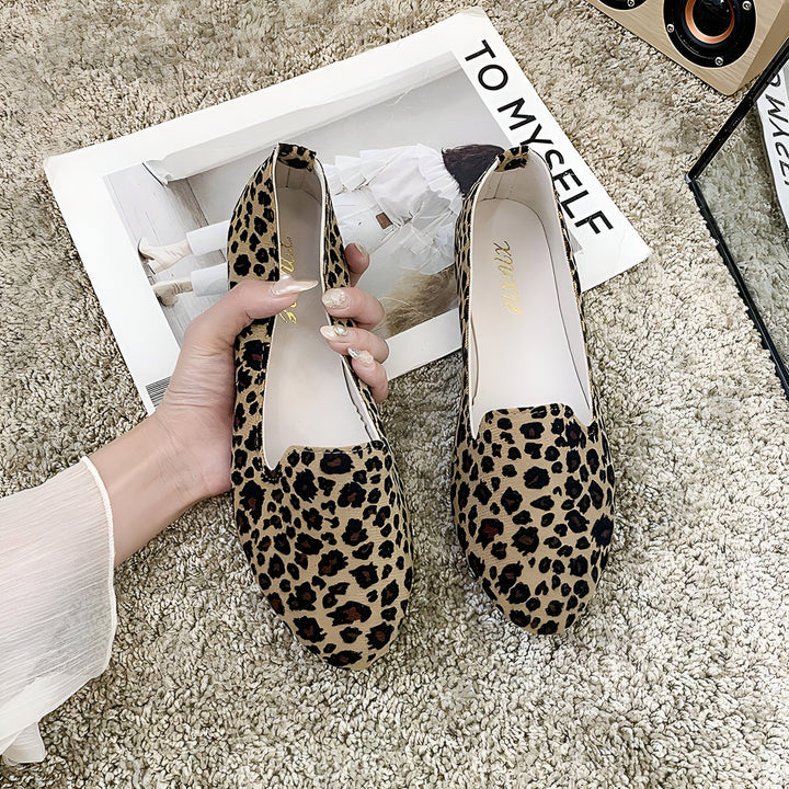 Chaussures plates à imprimé léopard sur un tapis texturé avec un magazine et un haut-parleur en arrière-plan. Une main tient une chaussure., 45287150485685,45287150518453,45287150551221,45287150583989,45287150616757,45287150649525,45287150682293,45287150715061,45287150747829