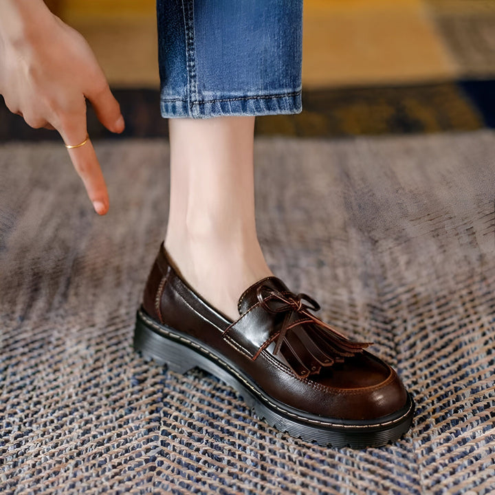 Gros plan sur une femme portant des mocassins marron à glands avec un jean. La femme pointe la chaussure avec un anneau d'or sur son doigt., 45286718308533,45286718341301,45286718374069,45286718406837,45286718439605,45286718472373,45286718505141,45286718537909,45286718570677,45286718603445,45286718636213,45286718668981,45286718701749,45286718734517