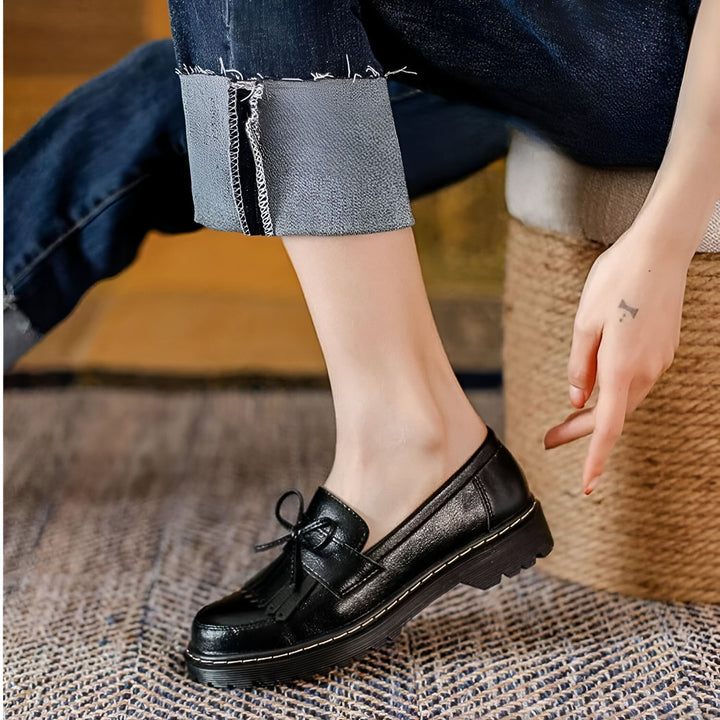 Gros plan d'une femme portant des mocassins noirs à glands et un jean retroussé, assise sur un tabouret en osier. La personne a un petit tatouage sur la main., 45286718308533,45286718341301,45286718374069,45286718406837,45286718439605,45286718472373,45286718505141,45286718537909,45286718570677,45286718603445,45286718636213,45286718668981,45286718701749,45286718734517