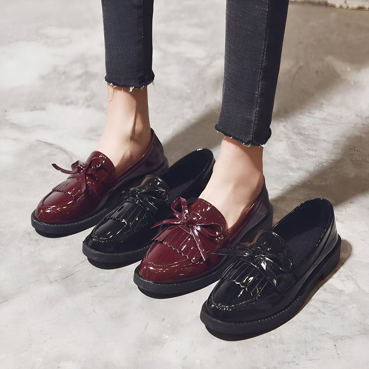 Chaussures mocassins vernis à franges et nœuds. Deux paires, une noire et une bordeaux, sont portées avec un jean noir. Mode femme, chaussures élégantes, style preppy., 45287001292981,45287001325749,45287001358517,45287001391285,45287001424053,45287001456821,45287001489589,45287001522357,45287001555125,45287001587893