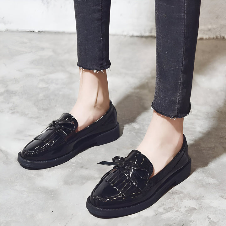 Mocassins noirs vernis pour femme, style preppy chic. Chaussures à glands avec nœud, portées avec un jean slim noir. Idée de tenue décontractée et élégante., 45287001292981,45287001325749,45287001358517,45287001391285,45287001424053,45287001456821,45287001489589,45287001522357,45287001555125,45287001587893