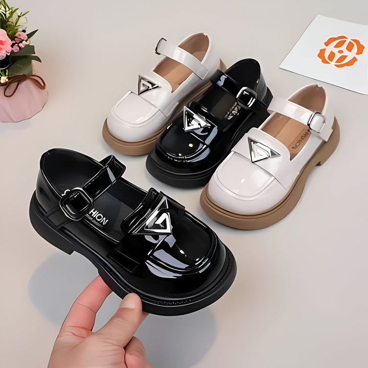 Quatre chaussures Mary Jane vernies pour enfants, une paire noire tenue à la main, avec une boucle et un triangle argenté décoratif. Les autres paires sont blanches et noires, sur une surface claire avec des fleurs. Chaussures d'école, mode enfantine., 45286683541685,45286683574453,45286683607221,45286683639989,45286683672757,45286683705525,45286683738293,45286683771061,45286683803829,45286683836597,45286683869365,45286683902133,45286683934901,45286683967669,45286684000437,45286684033205,4528668406597