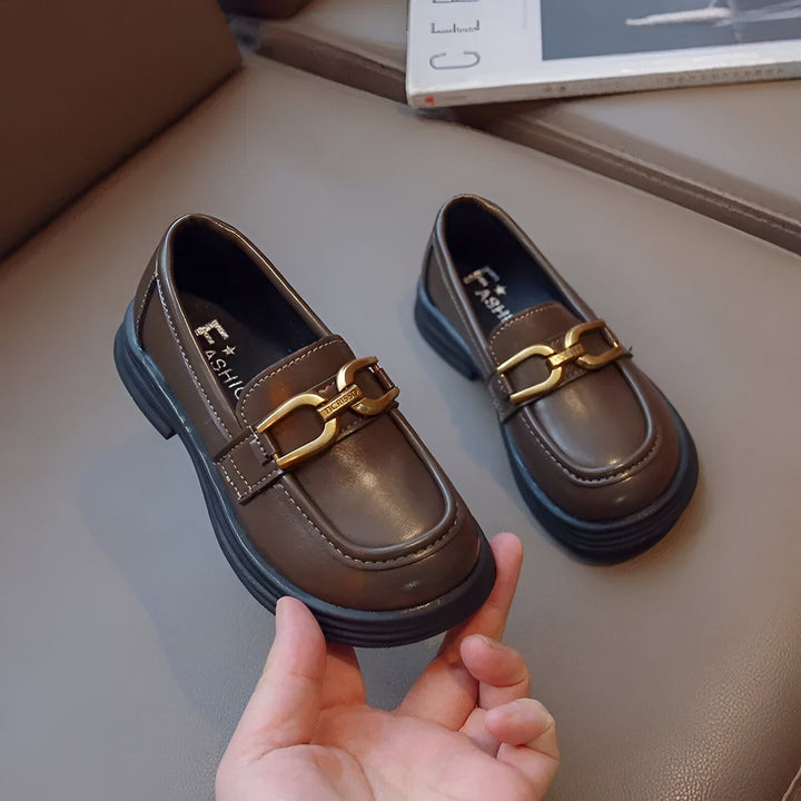 Chaussures mocassins marron avec une boucle dorée sur le dessus. Ces chaussures élégantes sont placées sur une surface rembourrée grise et sont idéales pour les enfants., 45286680953013,45286680985781,45286681018549,45286681051317,45286681084085,45286681116853,45286681149621,45286681182389,45286681215157,45286681247925,45286681280693,45286681313461,45286681346229,45286681378997,45286681411765,45286681444533