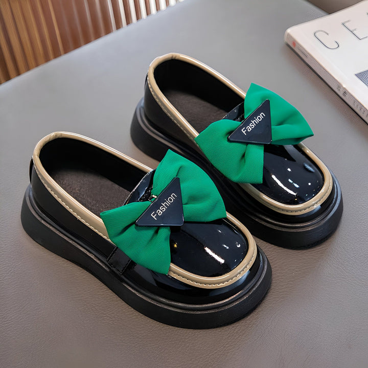 Deux mocassins vernis noirs pour enfant, ornés d'un nœud vert vif avec l'inscription "Fashion", sur une surface grise., 45287024033973,45287024066741,45287024099509,45287024132277,45287024165045,45287024197813,45287024230581,45287024263349,45287024296117,45287024328885,45287024361653,45287024394421,45287024427189,45287024459957,45287024492725,45287024525493,45287024558261,45287024591029,45287024623797,45287024656565,45287024689333,45287024722101,45287024754869,45287024787637,45287024820405,4528702485317