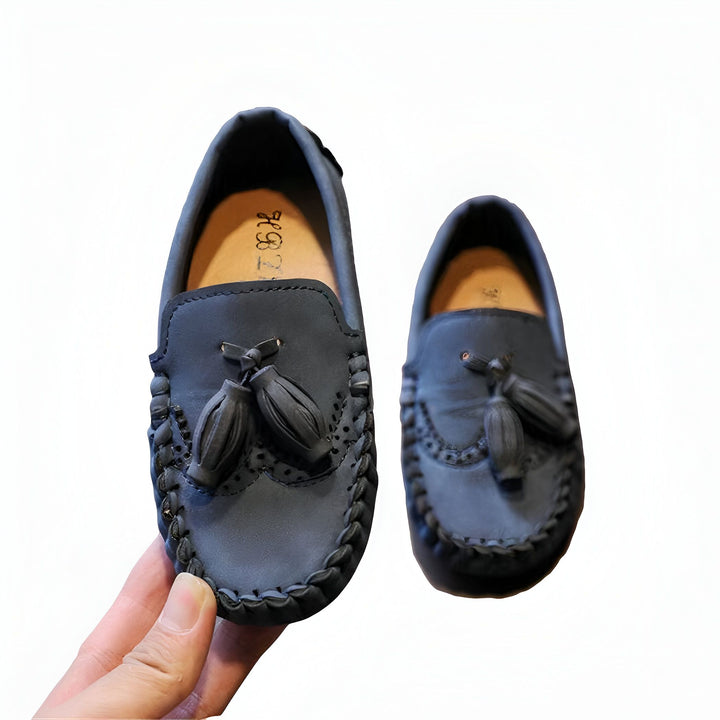 Mocassins pour enfant en cuir bleu marine avec pompons. Chaussures élégantes et confortables, idéales pour un look chic et décontracté. Main tenant une chaussure., 45286768607413,45286768640181,45286768672949,45286768705717,45286768738485,45286768771253,45286768804021,45286768836789,45286768869557