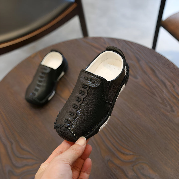 Chaussures de bébé en cuir noir sur table en bois, une main les tient. Mocassins confortables pour enfants, style décontracté et élégant. Mode enfantine, chaussures de qualité pour les petits pieds., 45286757826741,45286757859509,45286757892277,45286757925045,45286757957813,45286757990581,45286758023349,45286758056117,45286758088885,45286758121653,45286758154421,45286758187189,45286758219957,45286758252725,45286758285493,45286758318261,45286758351029,45286758383797,45286758416565,45286758449333,452