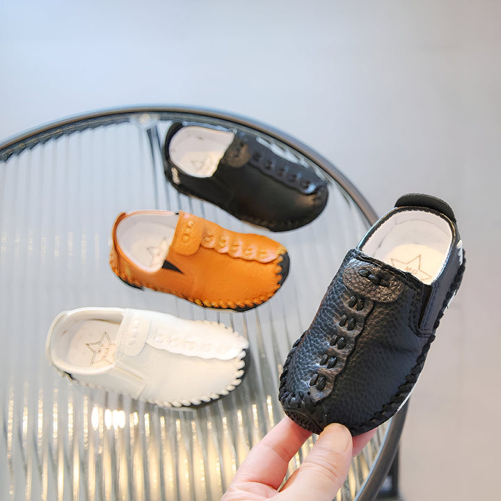 Chaussures pour enfants en cuir de différentes couleurs (noir, marron, blanc) disposées sur une table en verre. Un main tient une chaussure noire. Chaussures élégantes pour les petits. Mode enfantine., 45286757826741,45286757859509,45286757892277,45286757925045,45286757957813,45286757990581,45286758023349,45286758056117,45286758088885,45286758121653,45286758154421,45286758187189,45286758219957,45286758252725,45286758285493,45286758318261,45286758351029,45286758383797,45286758416565,45286758449333,4528