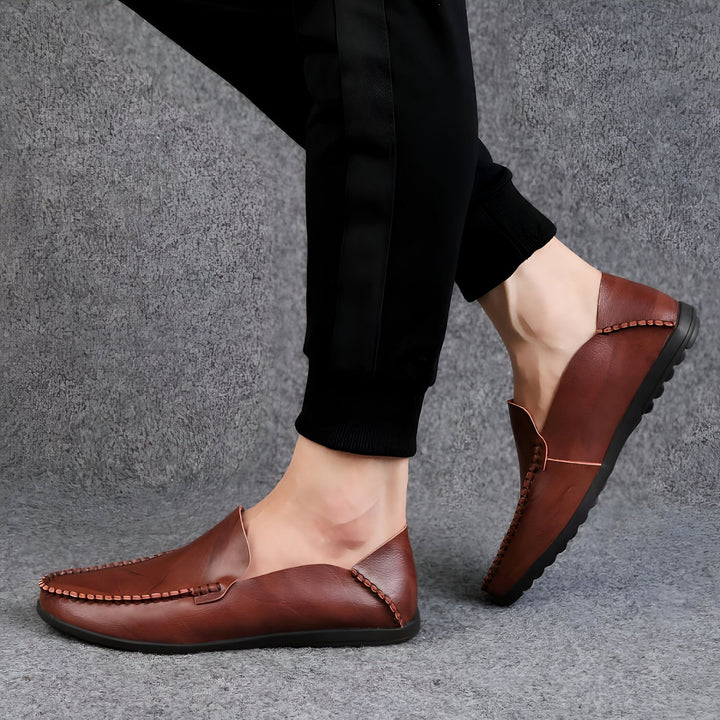 Gros plan sur une paire de mocassins en cuir marron portés avec un pantalon de survêtement noir sur un fond gris texturé. Chaussures décontractées et élégantes, parfaites pour un look moderne., 45287130169525,45287130202293,45287130235061,45287130267829,45287130300597,45287130333365,45287130366133,45287130398901,45287130431669,45287130464437,45287130497205,45287130529973,45287130562741,45287130595509,45287130628277,45287130661045,45287130693813,45287130726581,45287130759349,45287130792117,452871308
