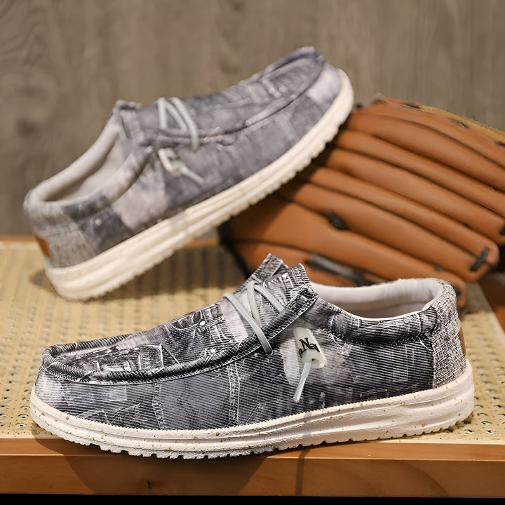 Deux mocassins décontractés en toile grise à motifs modernes, posés sur une table en bois, avec un gant de baseball en cuir brun en arrière-plan. Idéal pour un style décontracté et confortable., 45286670532789,45286670565557,45286670598325,45286670631093,45286670663861,45286670696629,45286670729397,45286670762165,45286670794933,45286670827701,45286670860469,45286670893237,45286670926005,45286670958773,45286670991541,45286671024309,45286671057077,45286671089845,45286671122613,45286671155381,4528667