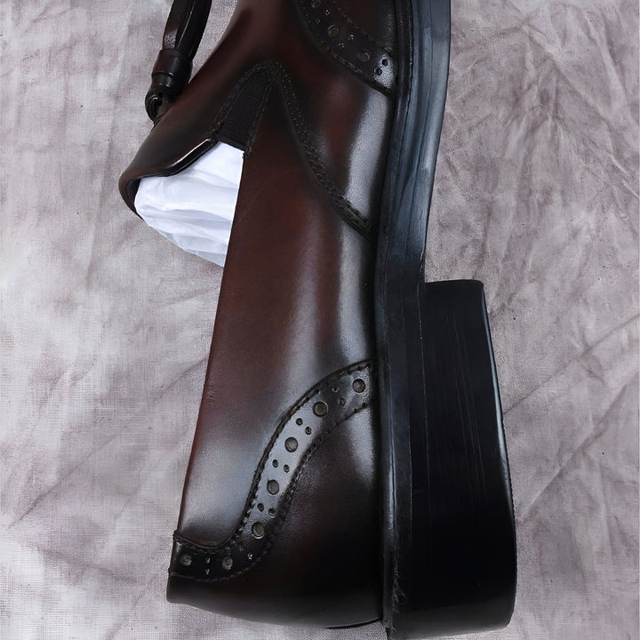 Vue rapprochée d'une botte Chelsea marron en cuir avec des détails perforés, un talon bloc noir et un élastique sur le côté. Le chaussant est visible., 45286843941045,45286843973813,45286844006581,45286844039349,45286844072117,45286844104885,45286844137653