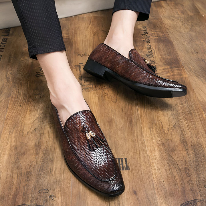 Gros plan sur des mocassins marron en cuir tressé avec glands dorés, portés par un homme en pantalon noir sur un parquet en bois. Chaussures élégantes et confortables., 45286928122037,45286928154805,45286928187573,45286928220341,45286928253109,45286928285877,45286928318645,45286928351413,45286928384181,45286928416949,45286928449717,45286928482485,45286928515253,45286928548021