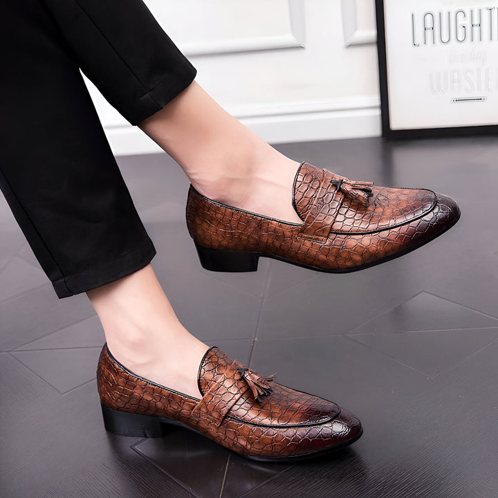 Homme portant des mocassins en cuir marron à motif crocodile avec glands, assis avec un pantalon noir. Chaussures élégantes pour hommes., 45287059423413,45287059456181,45287059488949,45287059521717,45287059554485,45287059587253,45287059620021,45287059652789,45287059685557,45287059718325,45287059751093,45287059783861,45287059816629,45287059849397,45287059882165,45287059914933,45287059947701,45287059980469,45287060013237,45287060046005,45287060078773,45287060111541,45287060144309,45287060177077,452870602
