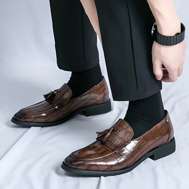 Gros plan sur des mocassins marron en cuir à motif crocodile, portés avec des chaussettes noires et un pantalon noir. On aperçoit une montre au poignet. Chaussures élégantes pour homme., 45286642286773,45286642319541,45286642352309,45286642385077,45286642417845,45286642450613,45286642483381,45286642516149,45286642548917,45286642581685,45286642614453,45286642647221,45286642679989,45286642712757,45286642745525,45286642778293,45286642811061,45286642843829,45286642876597,45286642909365,45286642942133,452