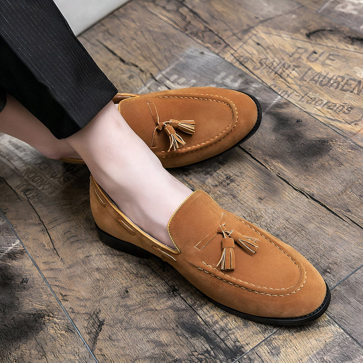 Gros plan de mocassins marron en daim avec glands, portés par une personne en pantalon noir sur un parquet en bois décoratif. Chaussures élégantes pour hommes., 45287110410421,45287110443189,45287110475957,45287110508725,45287110541493,45287110574261,45287110607029,45287110639797,45287110672565,45287110705333,45287110738101