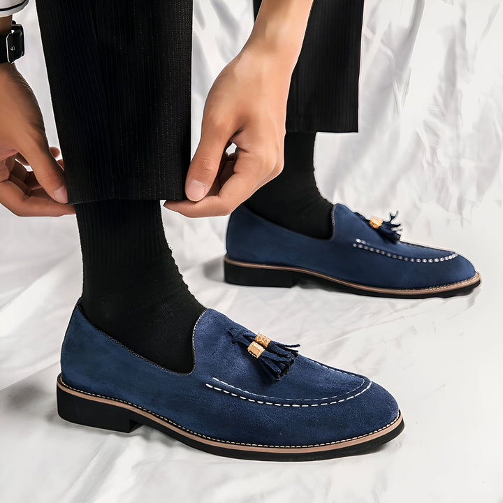 Homme ajustant son pantalon noir au-dessus de ses mocassins bleus en daim avec des glands, portés avec des chaussettes noires. Chaussures élégantes et confortables pour un look soigné., 45286848626869,45286848659637,45286848692405,45286848725173,45286848757941,45286848790709,45286848823477,45286848856245,45286848889013,45286848921781,45286848954549,45286848987317,45286849020085,45286849052853,45286849085621,45286849118389,45286849151157,45286849183925,45286849216693,45286849249461,45286849282229,45286